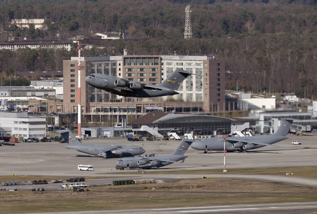 Ein Militärflieger startet, im Hintergrund ein Gebäude.