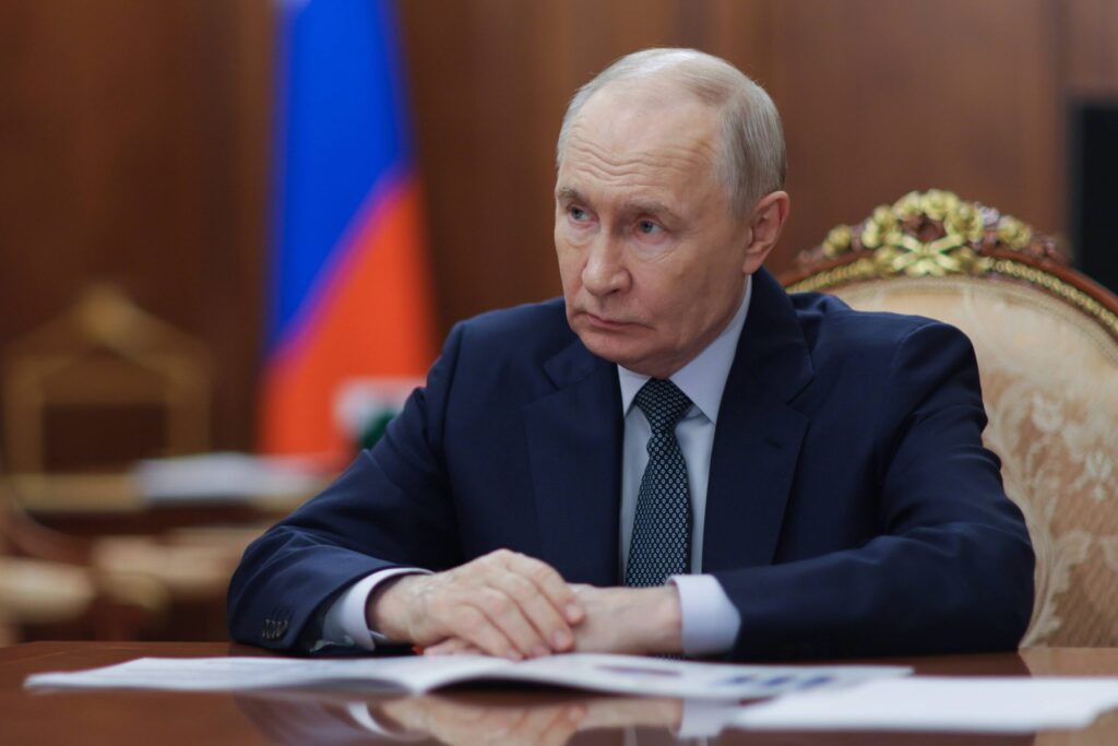 Ein Mann sitzt am Tisch, im Hintergrund die russische Flagge.