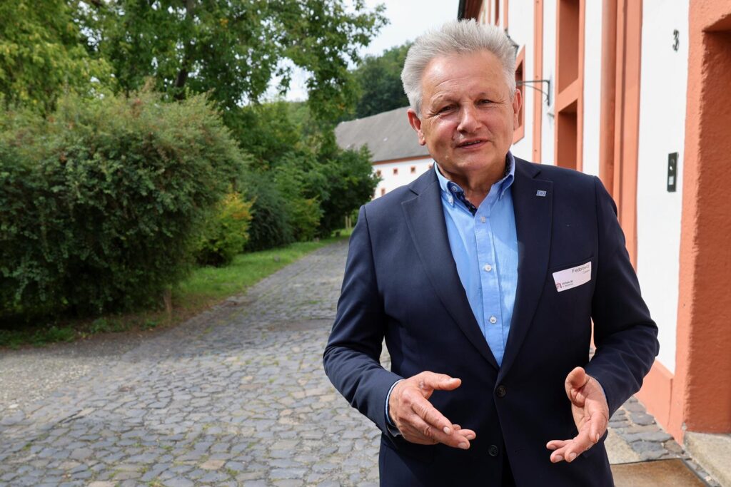 Ein Mann im Sakko schaut in die Kamera und gestikuliert.