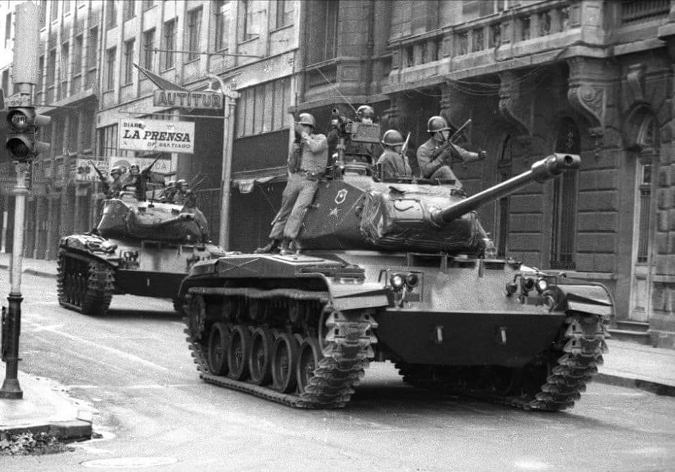 Das Schwarz-Weiß-Foto zeigt Panzer auf den Straßen der Stadt, auf denen bewaffnete Soldaten sitzen.