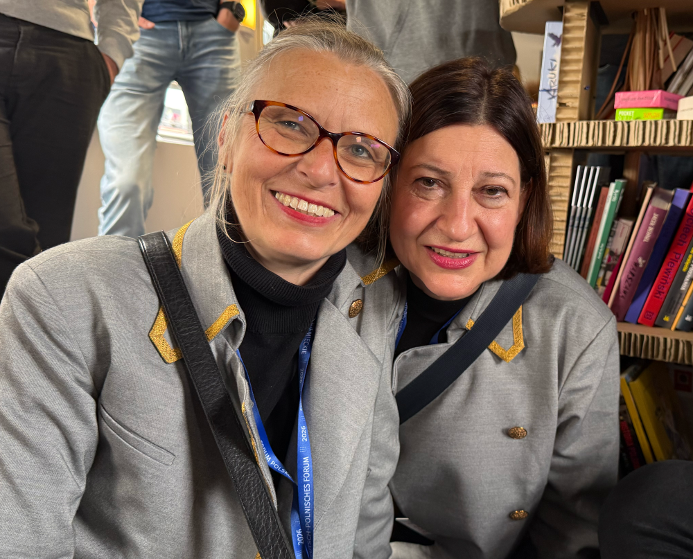 Zwei Frauen sitzen auf dem Boden eines Eisenbahnwaggons, neben ihnen ein Bücherregal.
