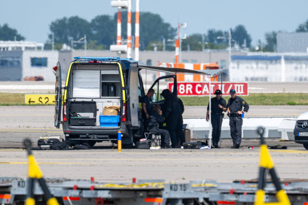 Polizisten arbeiten auf dem Rollfeld und stellen Teile der Drohne sicher
