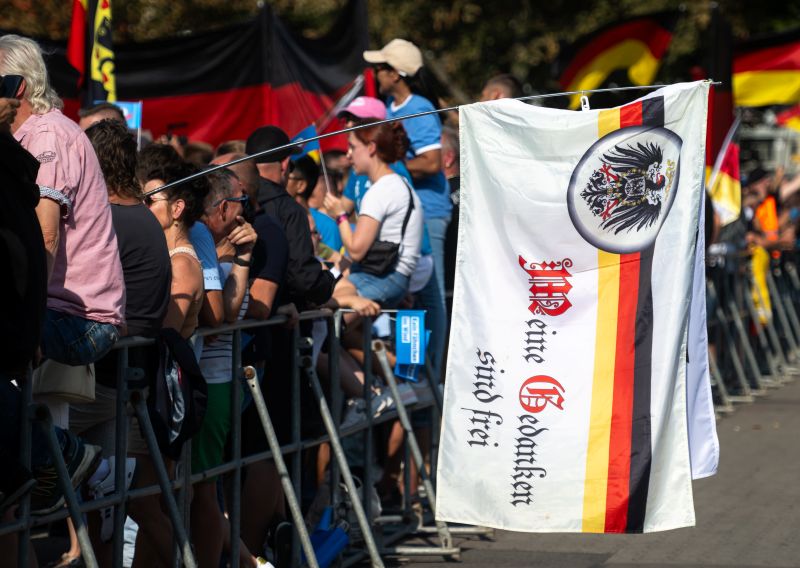 Eine Kundgebung, im Vordergrund eine Flagge mit dem deutschen Reichsadler und der Inschrift: Meine Gedanken sind frei. 