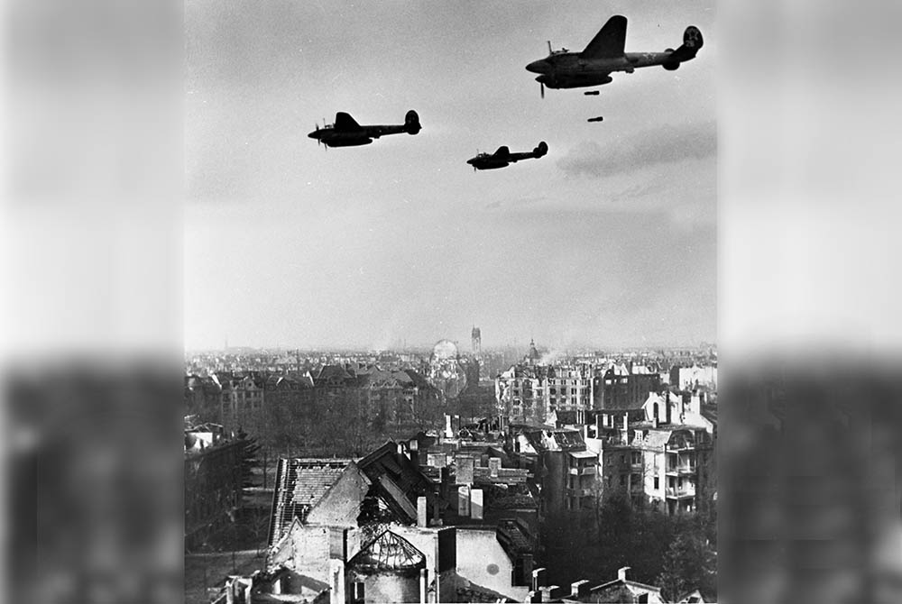 Das Schwarz-Weiß-Foto zeigt ein Flugzeug, das Bomben über einer Stadt abwirft.