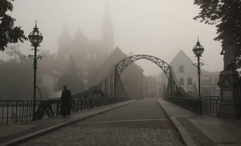 Das Foto zeigt eine Stadt im Nebel und eine Brücke, über die ein Mann geht.
