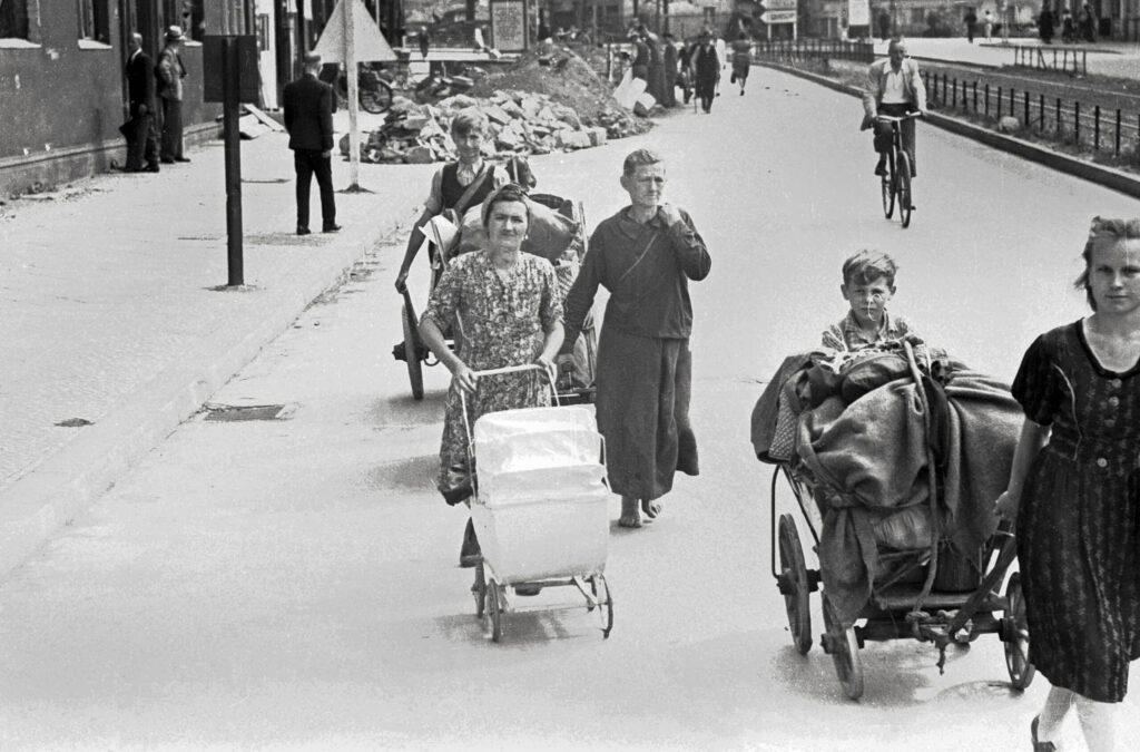 Das Schwarz-Weiß-Foto zeigt Menschen mit Handwagen auf den Straßen einer Stadt. 