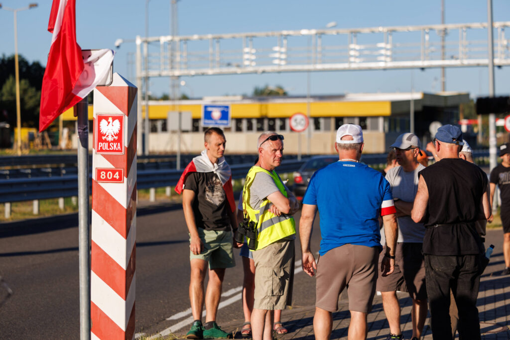 Männer in Sommerkleidung bewachen auf polnischer Seite den Grenzübergang Lubieszyn/Linken