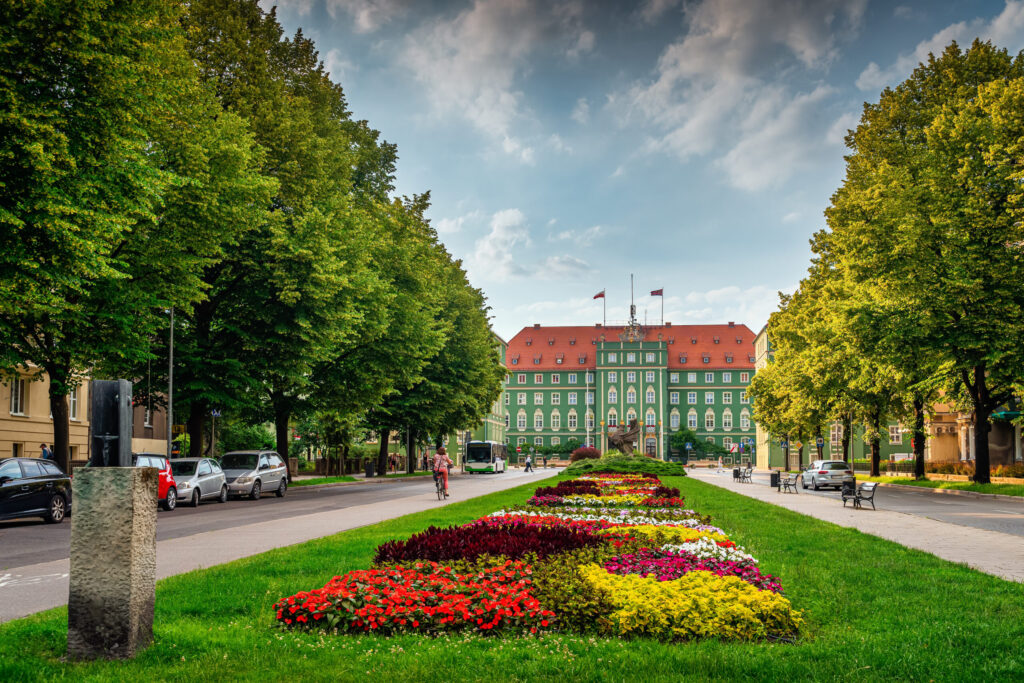 Ein Blumenbeet, Autos, ein Bus und eine Fahrradfahrerin vor der Stadtverwaltung in Stettin.