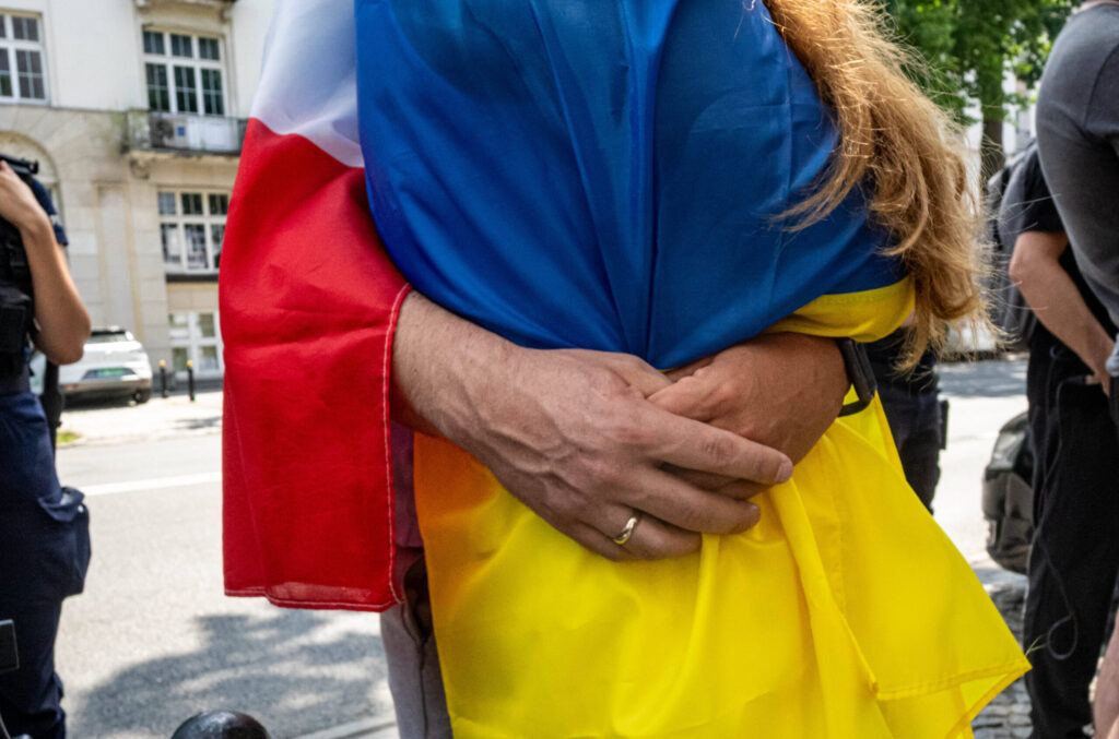 Zwei Menschen umarmen einander, sie sind in eine polnische und eine ukrainische Flagge gekleidet.