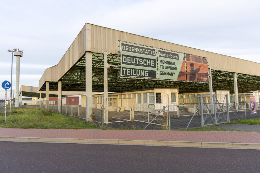 Ein großes Gebäude mit mehreren Schildern. Grenzübergang und Gedenkstätte.