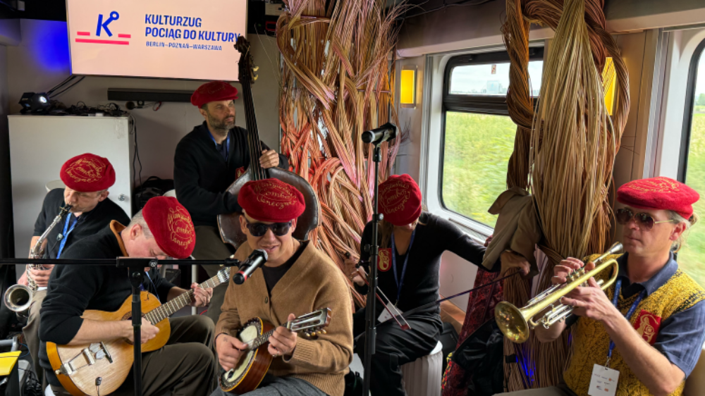 Eine Musikgruppe spielt in einem Zugwagen auf ihren Instrumenten.