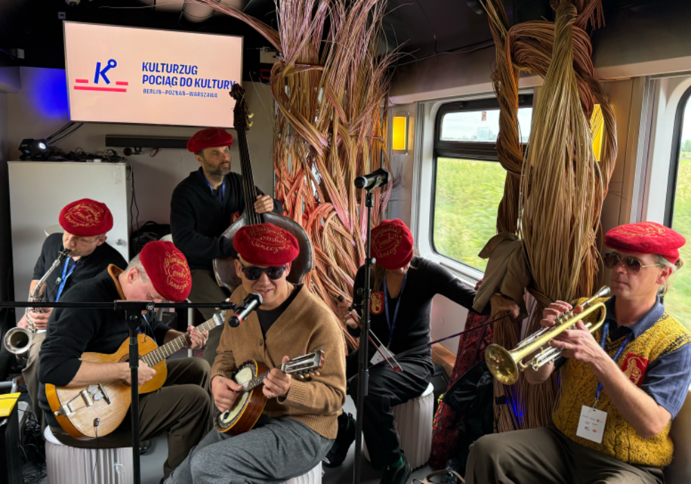 Eine Musikgruppe spielt in einem Zugwagen auf ihren Instrumenten.